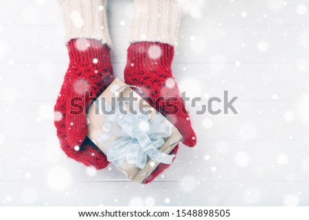 Hands in knitted mittens with gift box on white wooden table