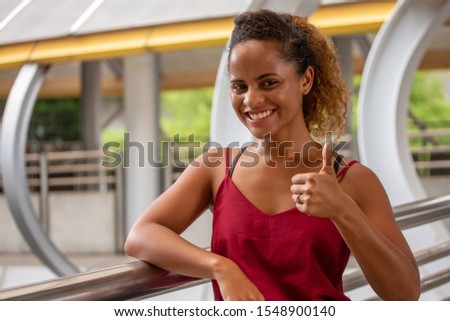 beautiful African American woman smiling and show thumbs up in urban city outdoors. happy black lady with positive gesture looking at  camera. good job and done wiht copy space.