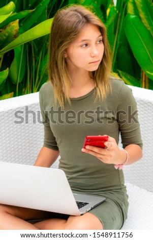 Young girl sitting outdoors with a laptop and a smartphone