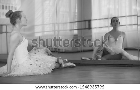 Young ballet dancer on a warm-up. The ballerina is preparing to perform in the studio. A girl in ballet clothes and shoes kneads by handrails.
