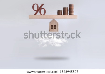 Percentage sign and stack of coins seasaw balanced on a miniature house hovering above the clouds, mortgage, investment concept