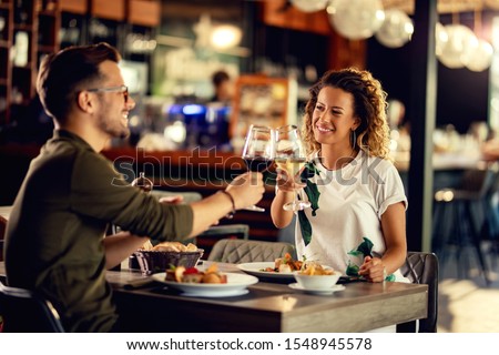 Young happy couple celebrating and toasting with wineglasses while eating in a restaurant.  Royalty-Free Stock Photo #1548945578