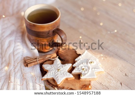 Christmas still life. Cup of tea, gingerbread glazed cookies, cinnamon at wooden background with glares. Cozy tea time with homemade sweets and mug of hot beverage. Winter food, drink, new year lights