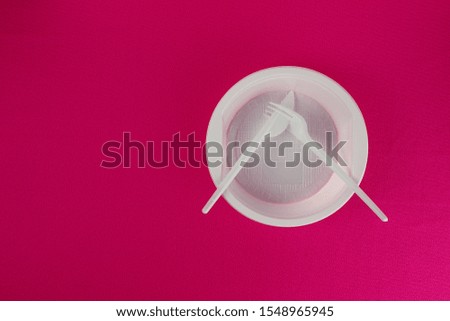 Disposable white plastic fork and knife lie crossed on a plate. Table setting