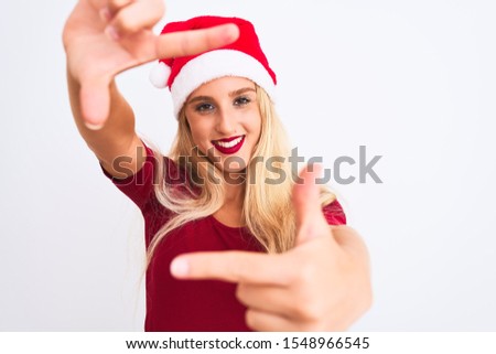 Young beautiful woman wearing Christmas Santa hat over isolated white background smiling making frame with hands and fingers with happy face. Creativity and photography concept.