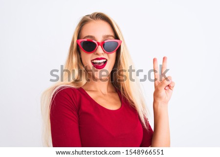 Young beautiful woman wearing red t-shirt and sunglasses over isolated white background smiling with happy face winking at the camera doing victory sign. Number two.