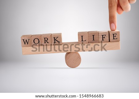 Close-up Of A Person's Finger Balancing Work And Life Blocks On Wooden Seesaw