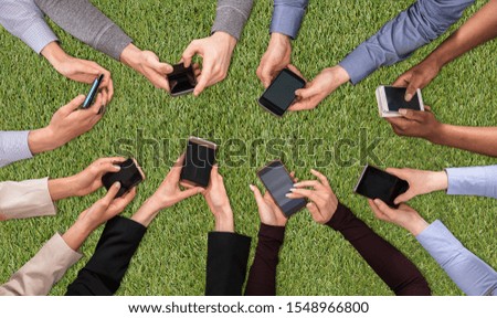 An Overhead View Of People's Hand Social Networking With Mobile Cellphones On Green Turf Background