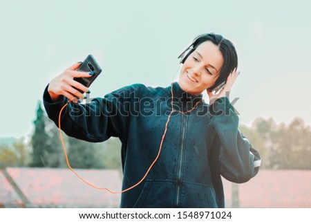 a girl in a tracksuit holding a phone and listening to music on the football stadium