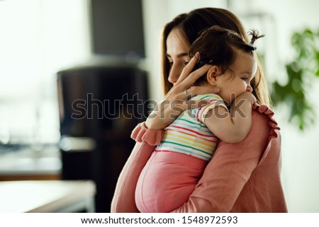 Affectionate mother embracing her baby daughter while holding her at home. Focus is on baby. 