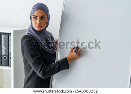 Strict Muslim teacher looking at students and about to write something on the paper board. Islam, education and school.