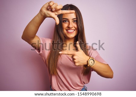 Young beautiful woman wearing t-shirt standing over isolated pink background smiling making frame with hands and fingers with happy face. Creativity and photography concept.