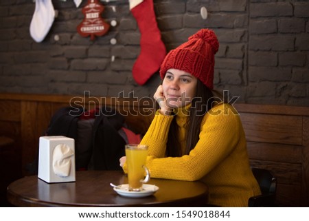 young happy woman in red hat winter outfit sitting in cafe drinking warm up tea