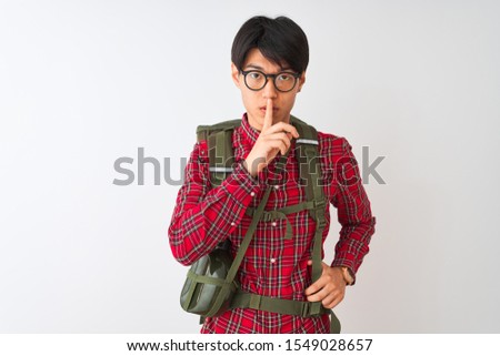 Chinese hiker man wearing backpack canteen glasses over isolated white background asking to be quiet with finger on lips. Silence and secret concept.