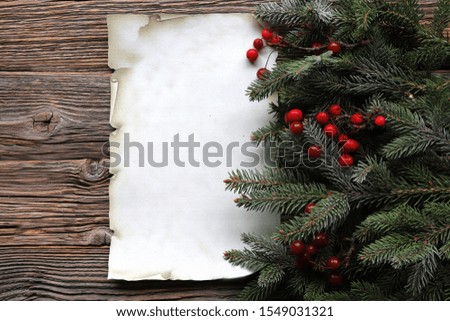 Christmas tree  branches with red berries and paper on wooden background 
