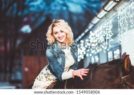 Blond girl with a horse in a sweater in winter. Against the background of bokeh from New Year's garlands