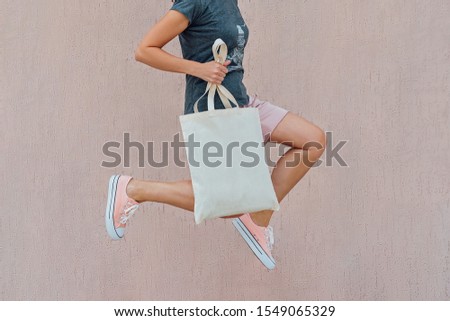 Woman in pink shorts and sneakers is jumping with white cotton bag in her hands. Mockup and zero waste concept.