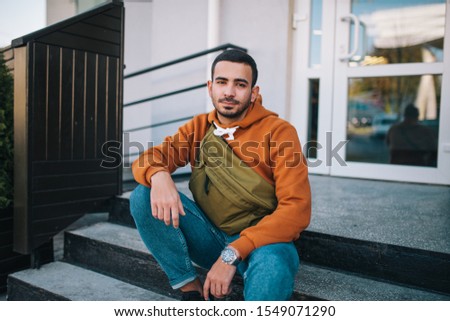 City portrait of handsome hipster guy wearing brown blank hoodie with big waist bag with space for your logo or design. Mockup for print