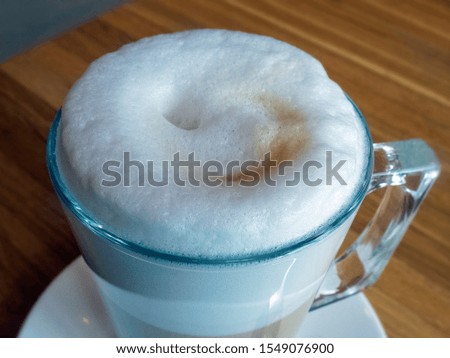 A latte coffee mug on the table close-up. The whipped milk on the surface of the coffee forms a lush foam. Foam rises above the mug