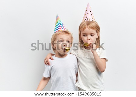 two cute children using party whistles, wearing party hats on a white background, happy childhood, close up portrait,holiday