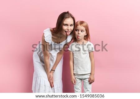 Close up portrait of careless pretty joyful funny mother and her daughter showing tongue, close eup portrait, isolated pink background, facial expression, reaction