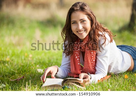 Beautiful young girl reading book while lying on grass 