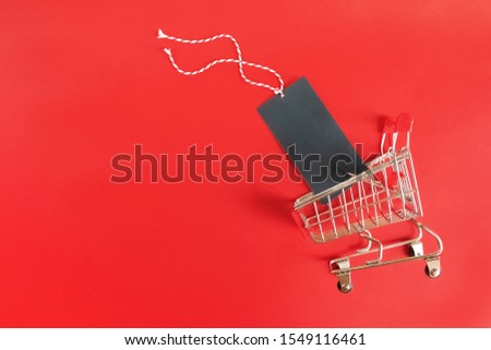 Little supermarket cart with empty black label on red background. Sale, black friday, cyber monday, online shopping concept.