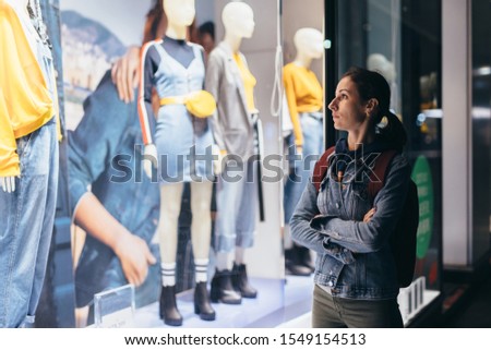 Girl stands outside the store and looks at the female clothes on the mannequins