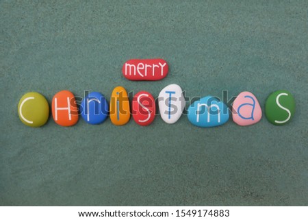 Merry Christmas text composed over green sand with creative colored stone letters 