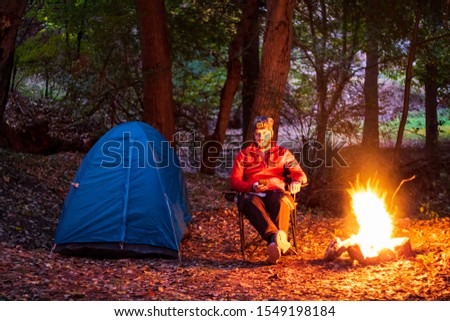 Camping in nature. Alone man sitting on the seat in front of the campfire. Camping in autumn. 