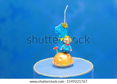 Number one candle on a blue background. Little prince theme. Fake birthday cake with personalized candle for first birthday for boy.