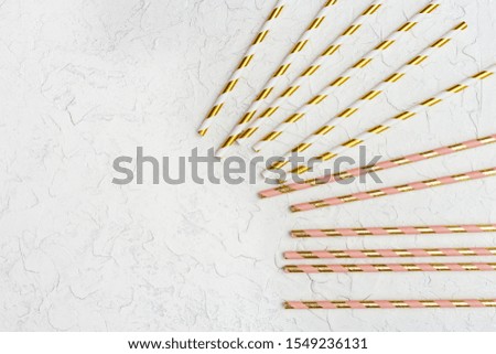 Bright paper drinking straws with golden striped pattern on shiny background with copy space. Concept for holiday or celebration. Flat lay. 