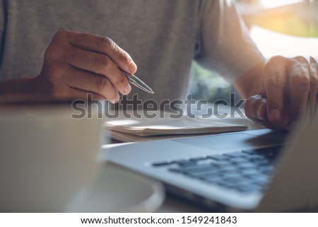 E-learning, online working. Casual business man writing with pen on notebook, searching internet, working on laptop computer with cup of coffee on table. Student studying online, lecturing on notepad