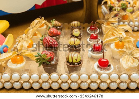 Different type of white chocolate candies covered by fruits. Grape strawberry and physalis. candies on a tray decorated with pearls. 