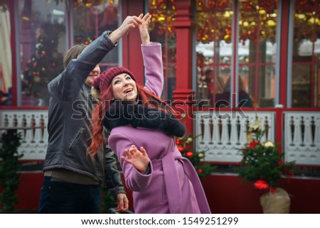 Meeting of lovers in city square, festively decorated for Christmas. Young people look at each other with love and tenderness and dance. Against backdrop of beautifully decorated Christmas trees