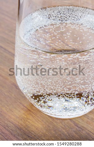 The water in the glass has bubbles placed on a wooden table, close-up view.