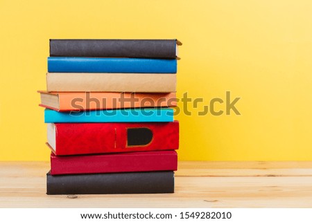 Simple Simple composition of many hardback books, unprocessed books on a wooden table and a yellow background. back to school. Copy space. Education.
