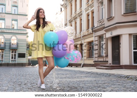 Beautiful young woman with color balloons on city street