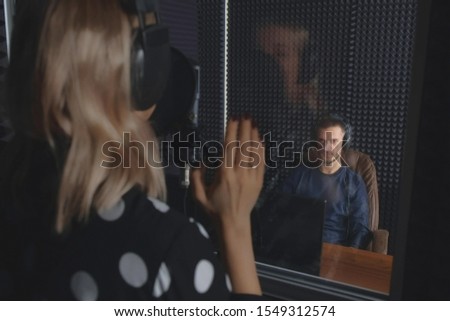 Man sound engineer in studio recording song of woman professional vocalist singer singing in microphone. Creating new melody audio composition on musical session at recording company.