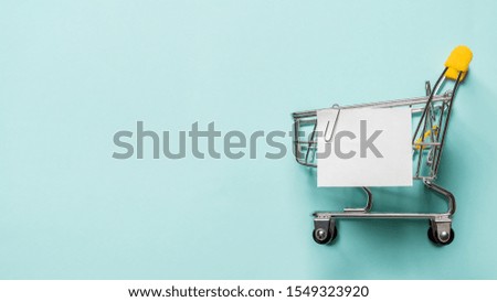 Shopping cart and white paper note list over blue background. Shopping concept on blue background. Empty white paper note over shopping cart. Copy space for text or design. Banner