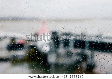 The rain drops on the window at the airport. Blur background picture of an airplane parking at the airport.    
