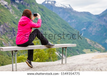 Tourism adventure and travel. Female tourist hiker sitting on bench in stone mountains taking photo with camera, looking at scenic view, Norway Scandinavia.