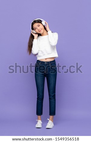Young pretty cute Asian woman smiling touching headphones and leaning head while listening to music  isolated on purple background
