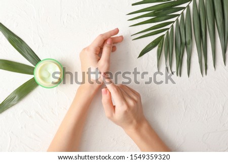 Young woman applying hand cream at light table Royalty-Free Stock Photo #1549359320