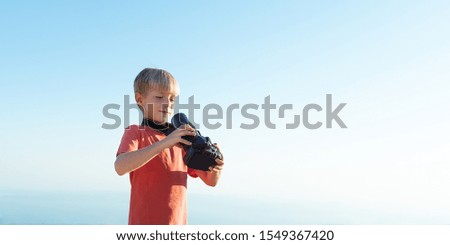 Kid with DSLR camera taking picture of himself, copy space. Child looking in the camera lens.