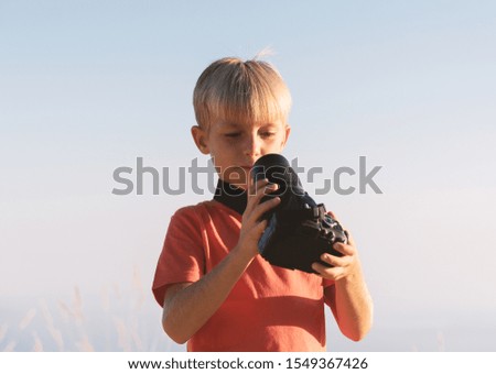 Kid with DSLR camera taking picture of himself. Curious child looking in the camera lens.