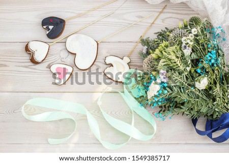 The concept of St. Valentine's Day and Wedding with a beautiful bouquet of wild flowers, white wooden photo background and heart shaped ginger cookies on sticks, top view