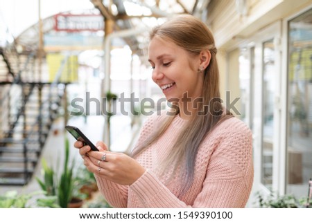 Internet and mobile phone. A young pretty blonde woman writes something on her smartphone and smiles.In the background, a city street. Close up