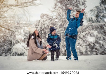 Beautiful family photo of mom with her two sons enjoying winter time. Playing with snow
