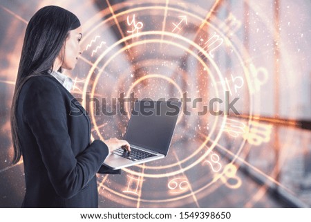 Attractive young european businesswoman with laptop and abstract zodiac sign hologram on blurry office interior background. Technology and astrology concept. Double exposure
